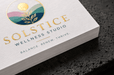 Stack of custom 12pt recycled uncoated business cards for Solstice Wellness Studio with gold foil stamped logo and botanical elements on dark stone