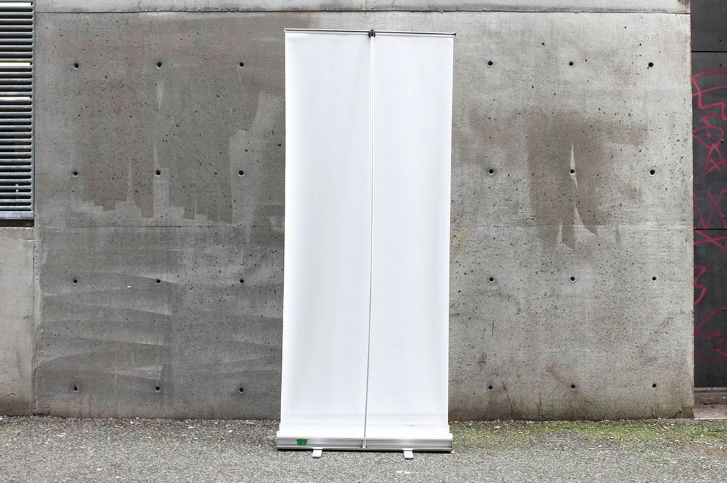 Back view of a 33x80 inch portable retractable banner stand displayed outdoors against a concrete wall. Clubcard Printing USA