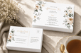 A stacked set of floral afternoon tea invitation cards and matching RSVP postcards featuring gold foil stamping, displayed on a textured cloth surface alongside a teacup, printed by Clubcard Palm Springs on 12pt 100% recycled fibers stock with full color detail.