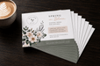 A fanned-out stack of printed coffee shop marketing cards on a dark wooden table next to a cup of latte art, printed by Clubcard Palm Springs on 12pt 100% recycled fibers stock with full color detail.